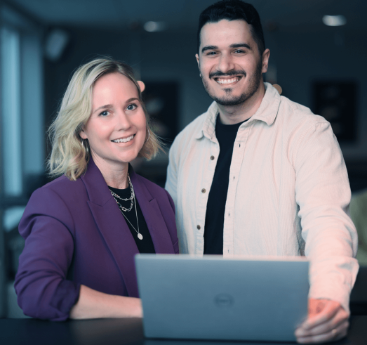 Foto p&aring; en kvinna och en man som st&aring;r framf&ouml;r en laptop med stora leenden mot kameran.