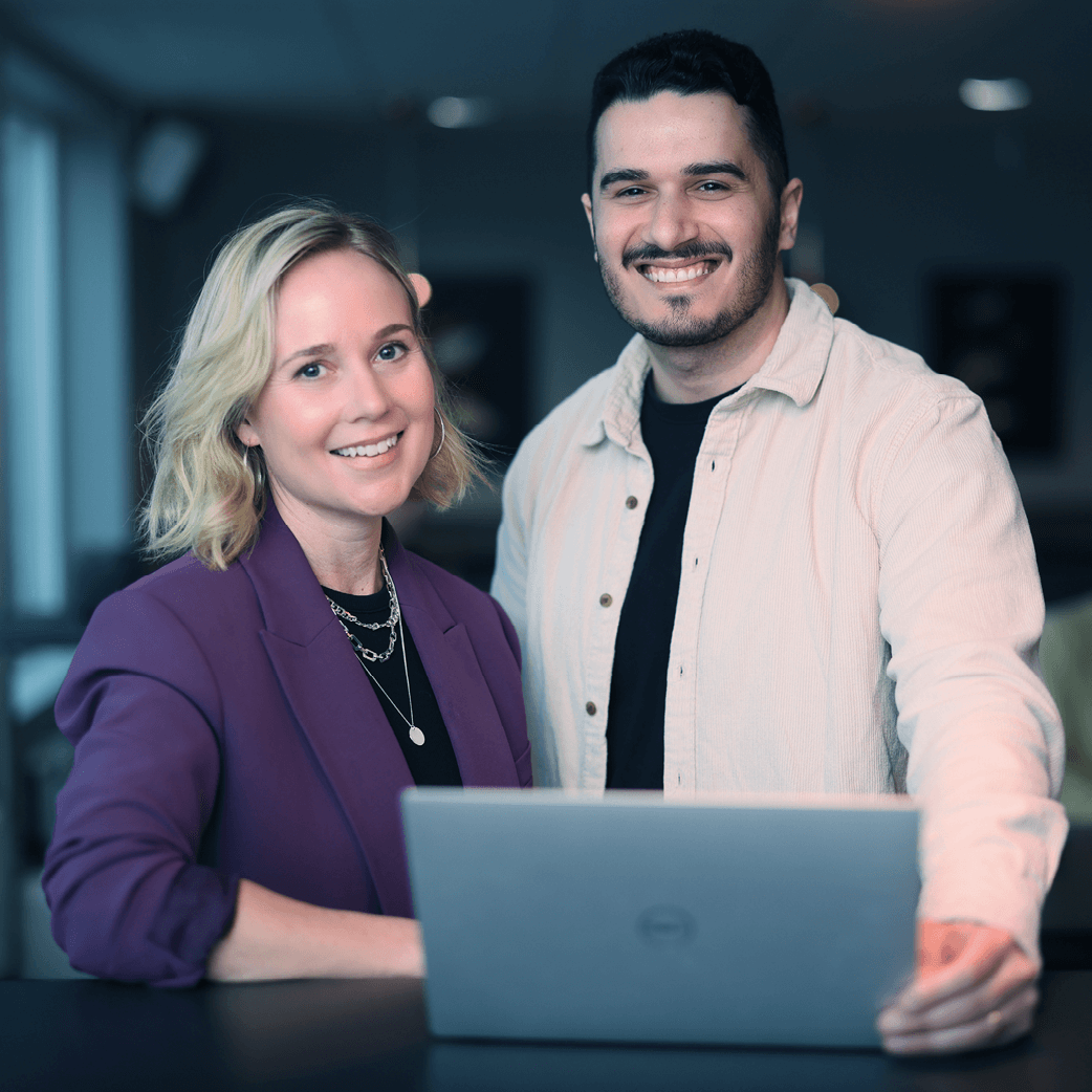 Foto p&aring; en kvinna och en man som st&aring;r framf&ouml;r en laptop med stora leenden mot kameran.